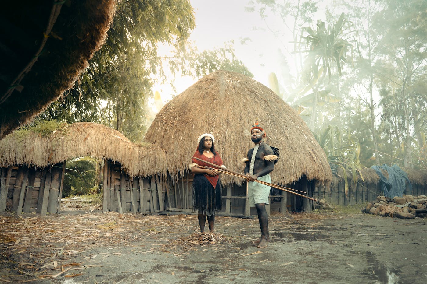 Two villagers in traditional attire standing in front of a thatched hut in a Melanesian village