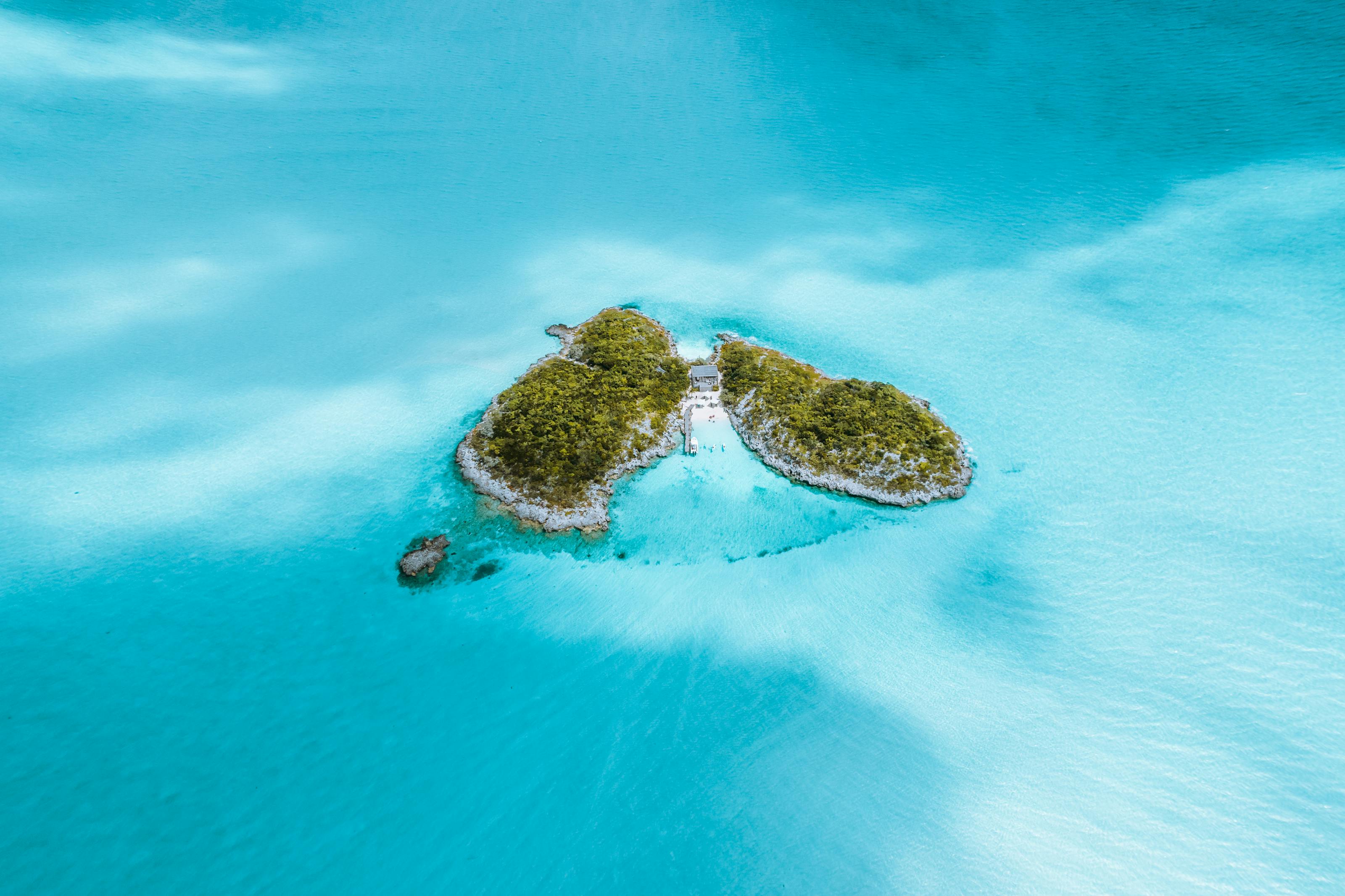 Aerial view of a green tropical island surrounded by turquoise ocean waters, evoking Vava‘u’s archipelago