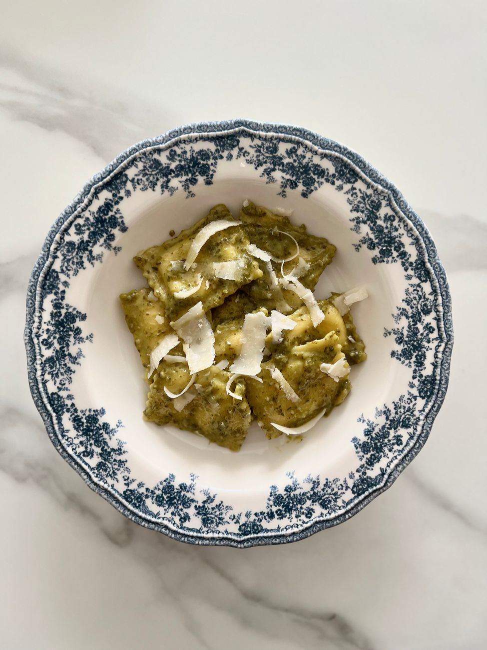 Ravioli with pesto sauce and shaved cheese in a patterned bowl