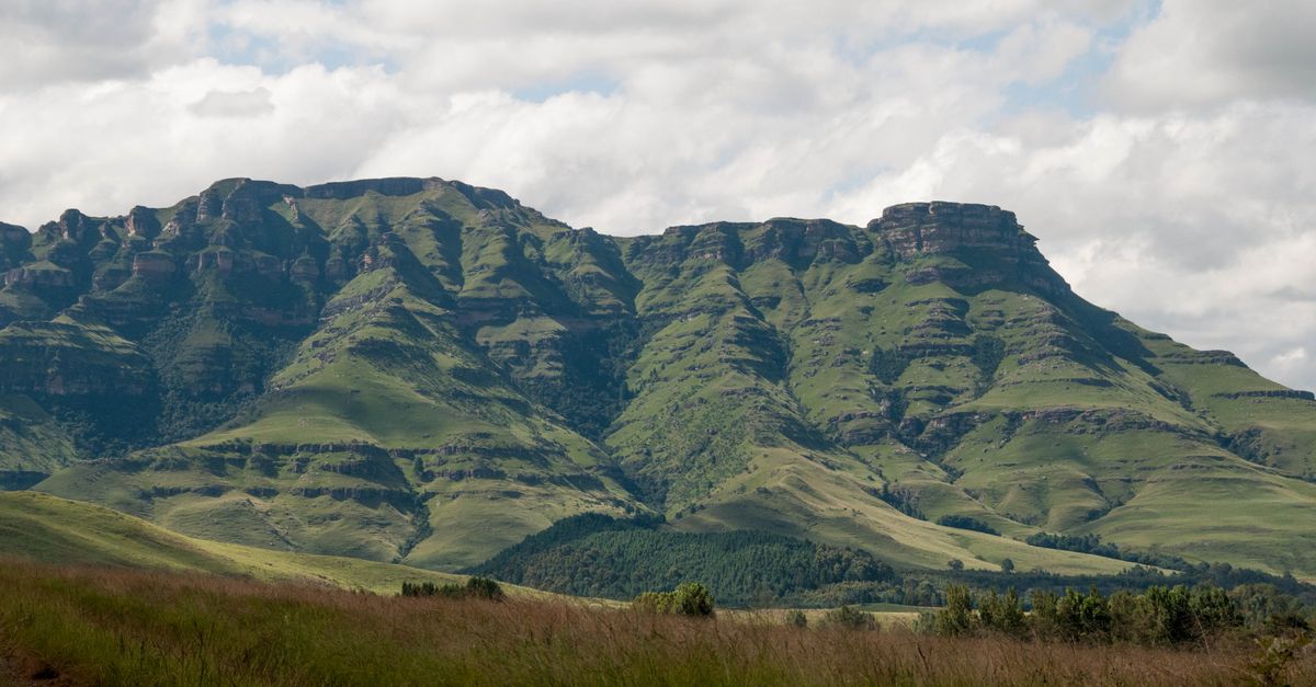The curved basalt wall of the Drakensberg Amphitheatre rising above green foothills