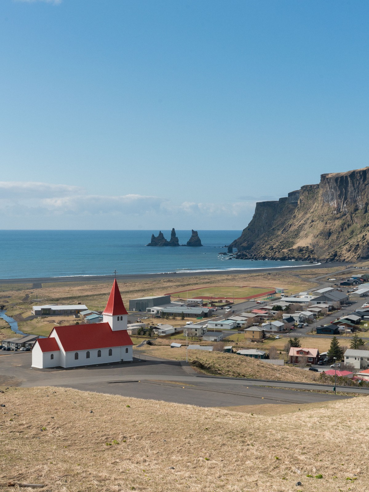 Red-roofed white church on a hill above the black beach at Vík í Mýrdal