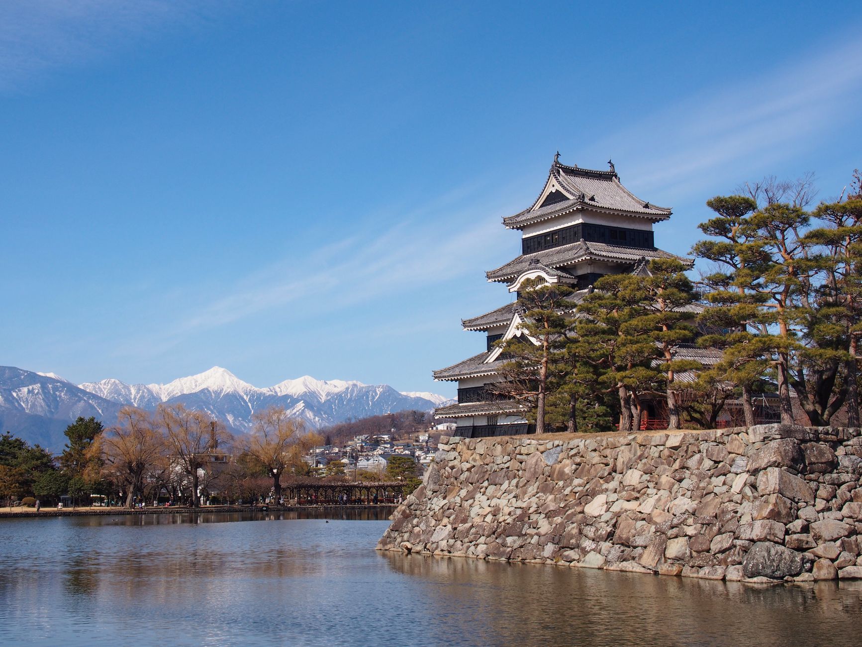 The black keep of Matsumoto Castle reflected in its moat with mountains behind