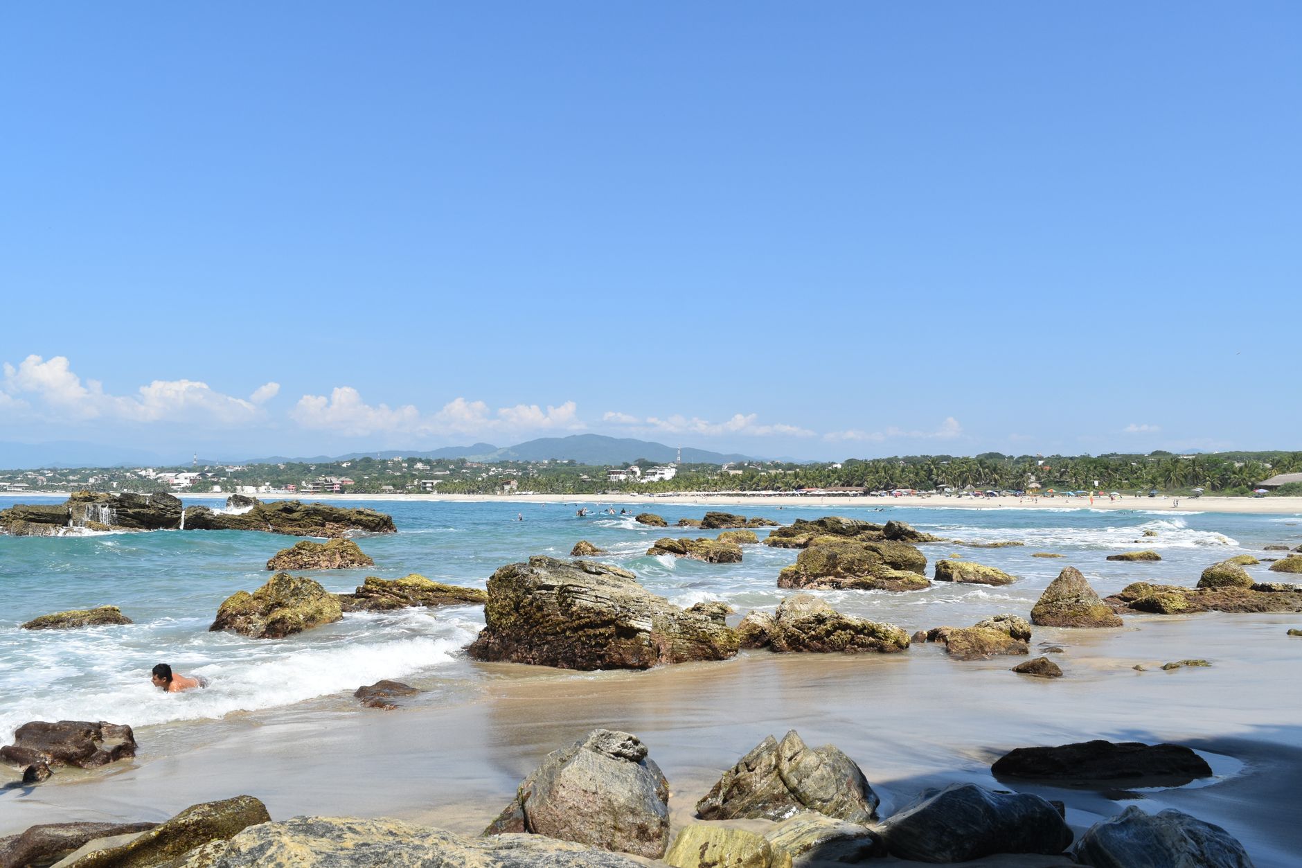 Big Pacific wave breaking at Playa Zicatela with dark sand and surfers in the lineup at Puerto Escondido