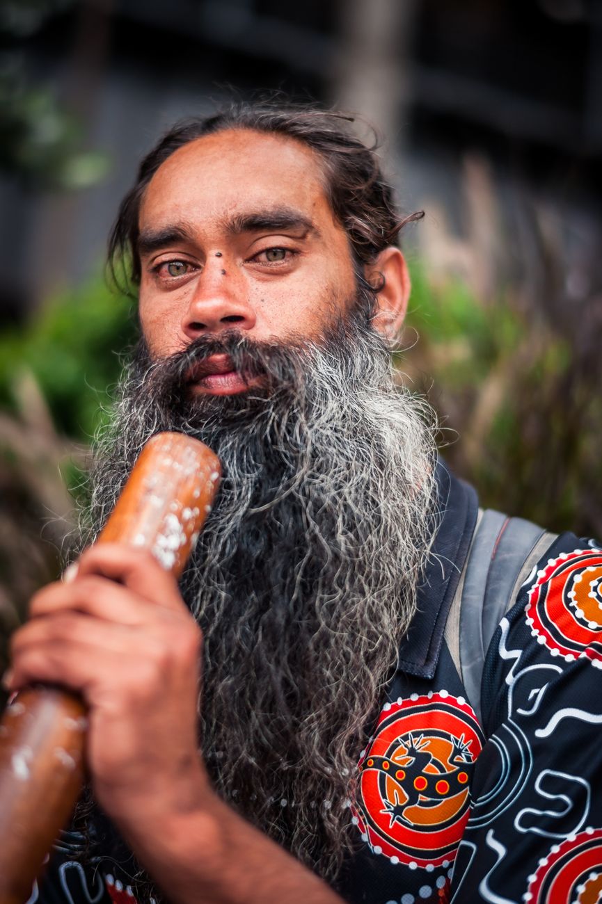 Indigenous Australian man playing didgeridoo in traditional patterned clothing