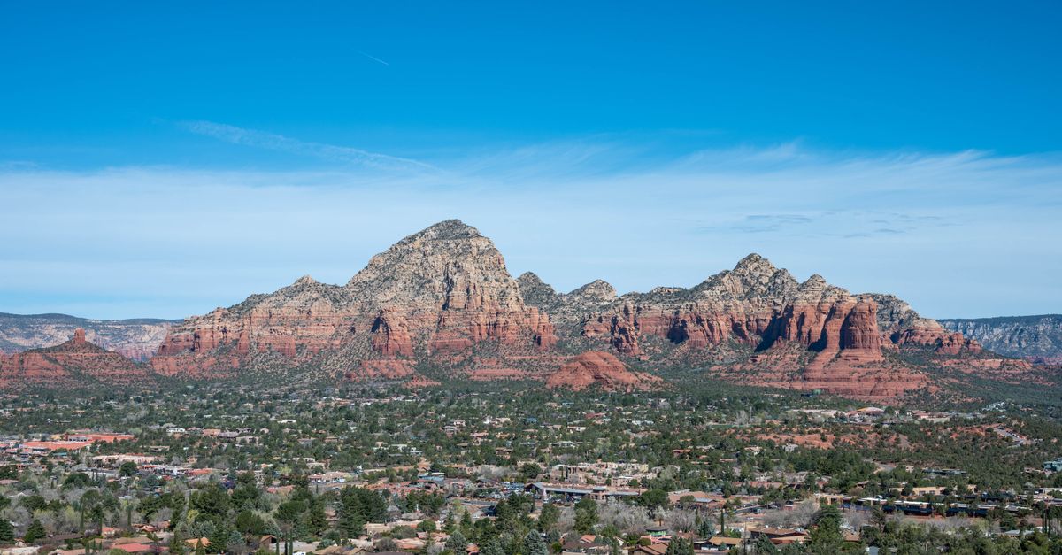 Red rock buttes rising directly behind the rooftops of Sedona at golden hour