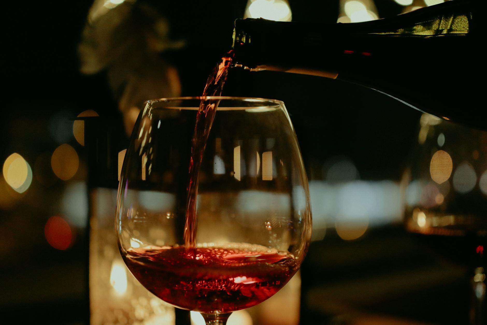 Close-up of red wine being poured into a glass with blurred lights in the background