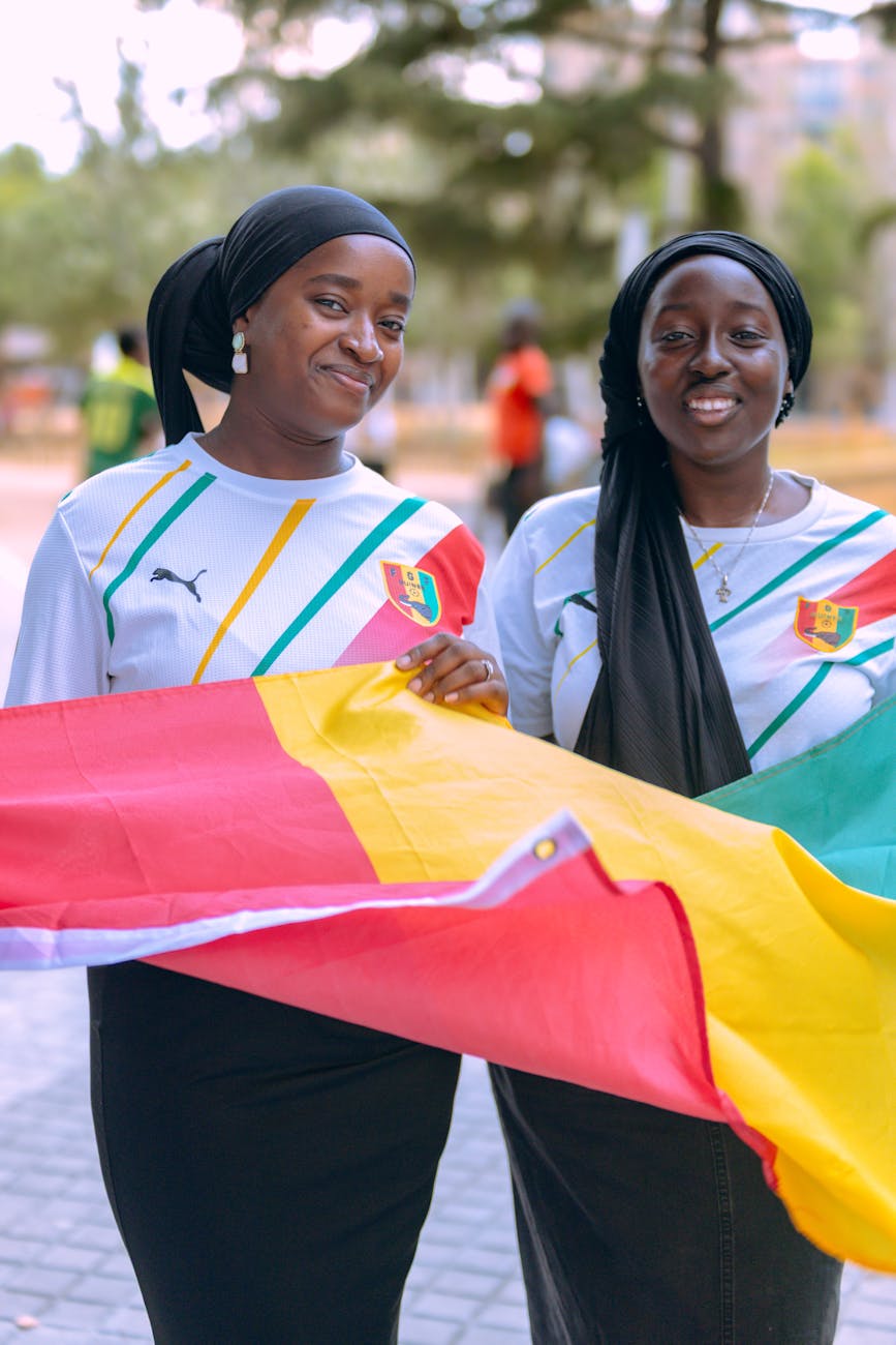 Two smiling women holding a Senegal flag outdoors in a cheerful setting